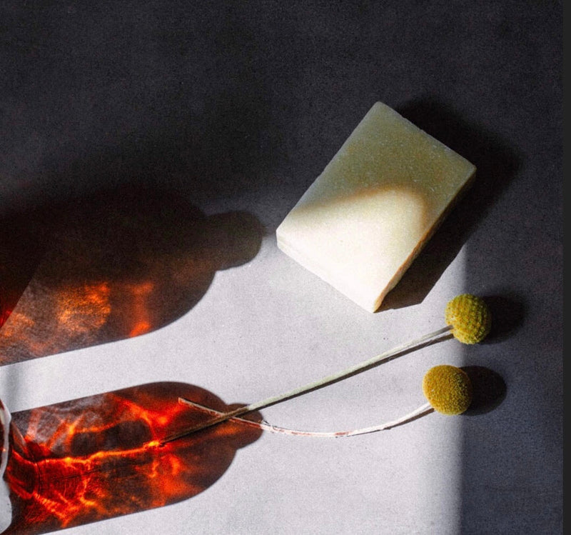 moody aesthetic photo of soap with amber glass bottle and flower